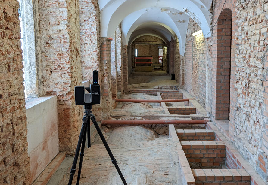 Ein Laserscanner steht auf einem Stativ in einem historischen Gewölbegang und erfasst die Umgebung für eine präzise digitale Vermessung des Gebäudes.