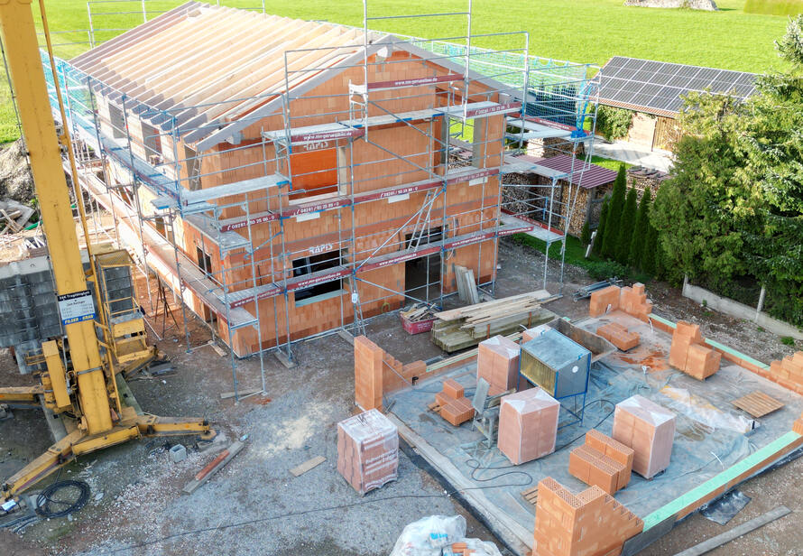 Drohnenaufnahme einer Baustelle mit Rohbau eines Einfamilienhauses. Sichtbar sind Gerüst, Kran und Baumaterialien für die Dokumentation des Baufortschritts.