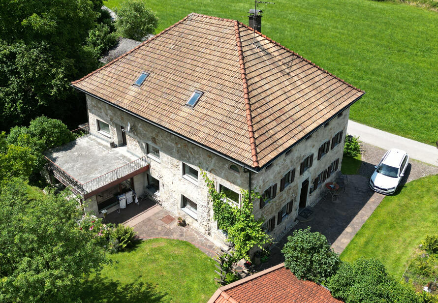Luftaufnahme eines Einfamilienhauses mit Garten und umliegender Landschaft. Ideal zur Immobilienvermarktung und zur Darstellung von Lage und Grundstück.