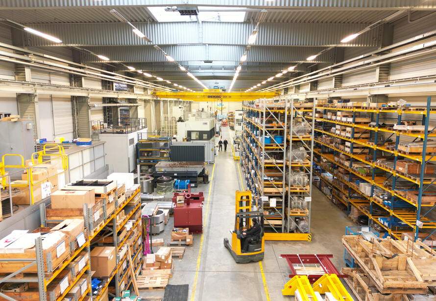 Innenaufnahme einer Industriehalle mit Regalsystemen, Maschinen und Logistikbereichen. Dokumentation von Produktions- und Lagerflächen aus erhöhter Perspektive.