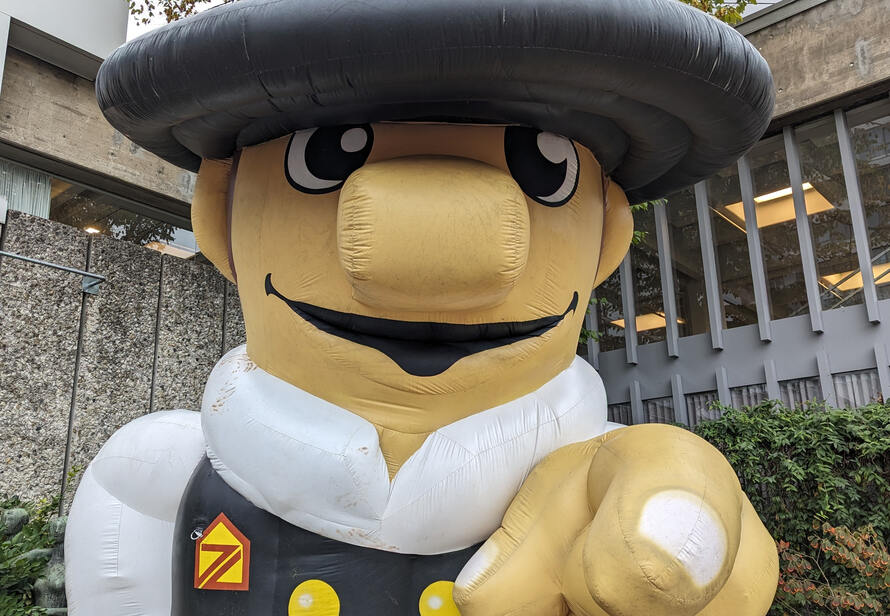 Zimmerer Maskottchen auf dem Holzbaugewerbetag als Symbol für das Handwerk, Tradition und die Verbindung zur modernen Digitalisierung im Bauwesen.