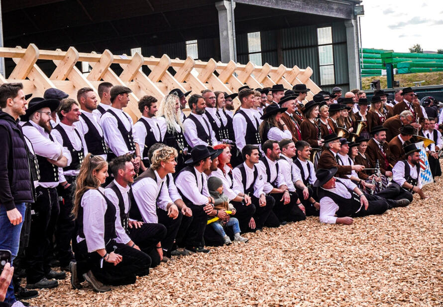 Gruppenfoto beim Zimmerer Treffen 2025 in Landau an der Isar mit über 1.100 Teilnehmern und traditioneller Handwerkskleidung vor einem aufgebauten Dachstuhl.