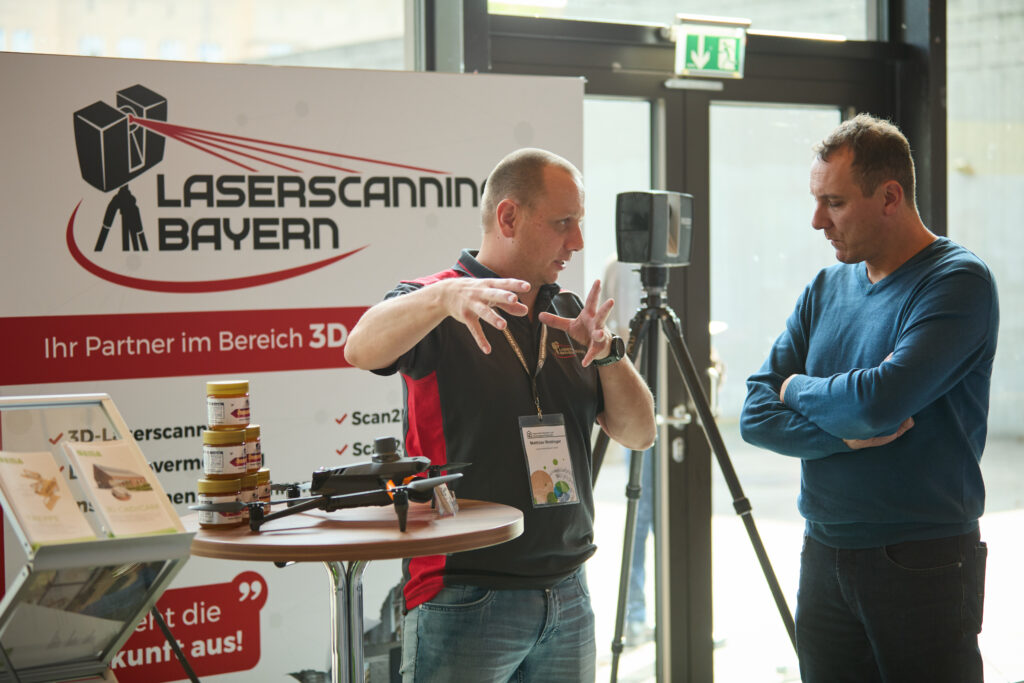 Matthias Weidinger erklärt am Messestand von Laserscanning Bayern einem Teilnehmer des Bayerischer Zimmerer- und Holzbaugewerbetag die 3D-Vermessung